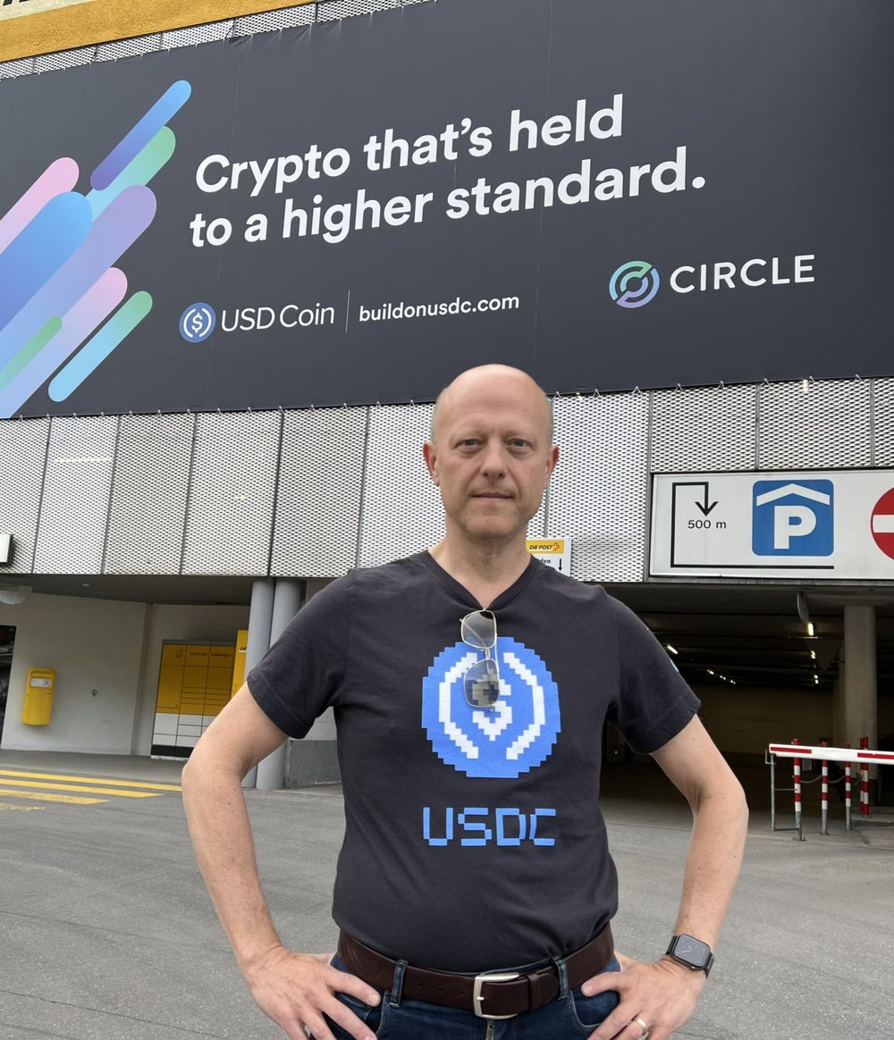 Circle CEO Jeremy Allaire wearing a pixel art USDC shirt in front of a Circle billboard